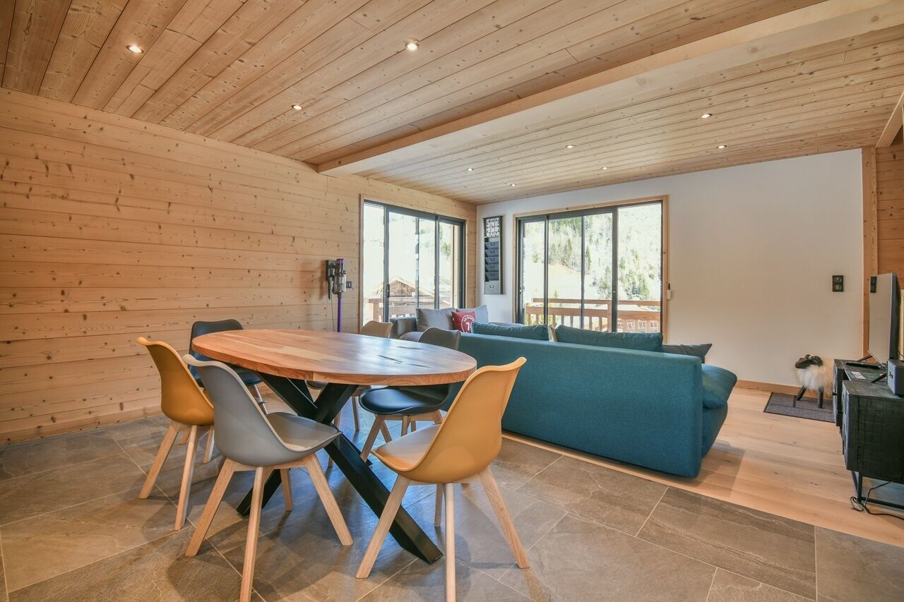 Un intérieur moderne avec un plafond en bois, une table de salle à manger ronde entourée de chaises, un canapé bleu et de grandes fenêtres.