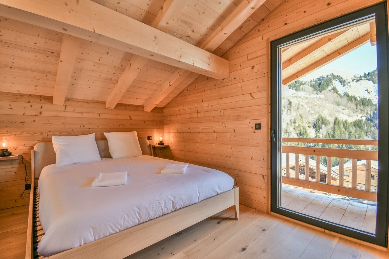 Une chambre à coucher située dans une cabane en bois, avec un lit, des tables de chevet et une grande fenêtre donnant sur une vue imprenable sur une montagne.