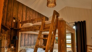 Una cama litera con escalera de madera, una lámpara de noche y una ventana con cortinas.