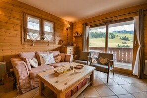 A cozy wooden cabin interior with a sofa, a table, and a chair. - Village Lessy - Apt Milou (Le Grand Bornand)