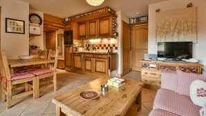 A cozy kitchen with wooden cabinets, a dining table with chairs, a TV, and a sofa.