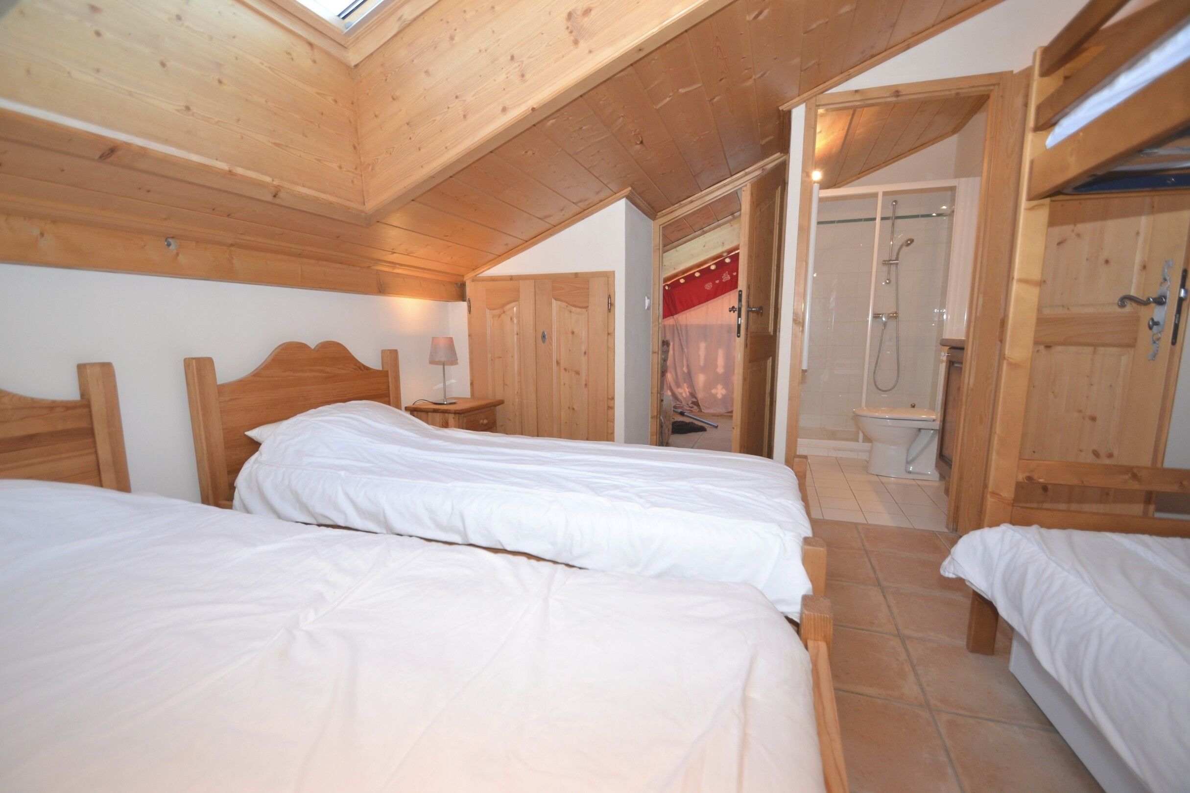 Un dormitorio con dos camas, paredes de madera, un tragaluz y una zona de ducha.