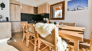 Eine moderne Küche mit Holzausstattung, eine Essecke mit Holztisch und -stühlen sowie ein großes Fenster mit Blick auf Berge und eine Seilbahn.