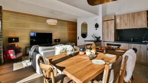 Ein modernes Wohnzimmer mit Esstisch aus Holz, einer Couch und einem Fernseher.