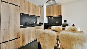 Eine moderne Küche mit Holzausstattung, einer schwarzen Arbeitsplatte und einem Essbereich mit einem weißen, flauschigen Tisch und Stühlen.