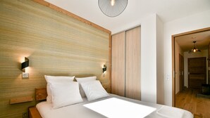 Ein modernes Schlafzimmer mit einem Holzkopfteil, zwei Nachttischlampen, einem großen Bett mit weißer Bettwäsche und einem Holzschrank.