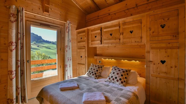 Quarto de cabana de madeira com uma cama, almofadas de bolinhas e recortes em formato de coração nas paredes.