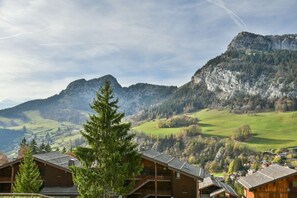 A mountain landscape with a prominent peak, a forested area, and a cluster of wooden buildings with balconies.