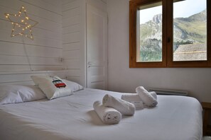 A hotel room with a bed, pillows, a star-shaped light fixture, a window with a mountain view, and a towel on the bed.