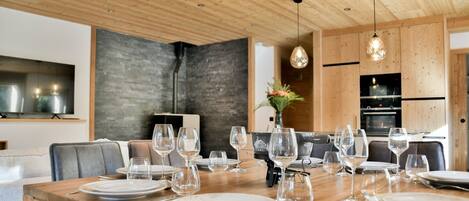 Un comedor con una mesa de madera dispuesta para una comida, una cocina moderna al fondo y una pared de acento de piedra.