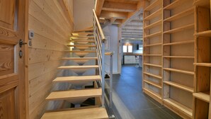 A wooden spiral staircase with metal railings, leading to a room with a kitchen area in the background.