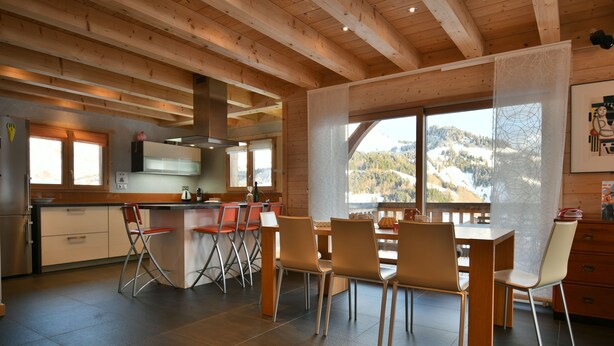 A modern kitchen with wooden beams, a dining area with chairs, and a view of a snowy mountain.