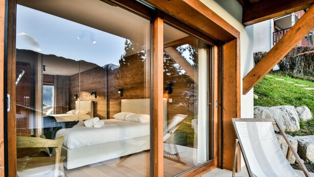 Un dormitorio moderno con una cama grande, una puerta de vidrio que da a un balcón y vistas al exterior.