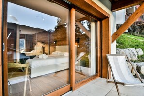 A modern bedroom with a large bed, a glass door leading to a balcony, and a view of the outdoors.