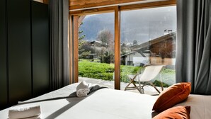 Un dormitorio con una ventana grande, una cama, una silla y vistas a un paisaje montañoso.