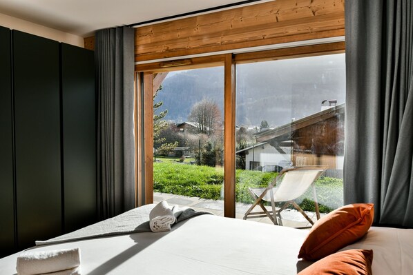 A bedroom with a large window, a bed, a chair, and a view of a mountainous landscape.