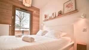 A bedroom with a wooden headboard, a large window, and a shelf with framed pictures.