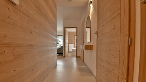 A hallway with wooden panel walls and a tiled floor, leading to a room with a bed and a window.