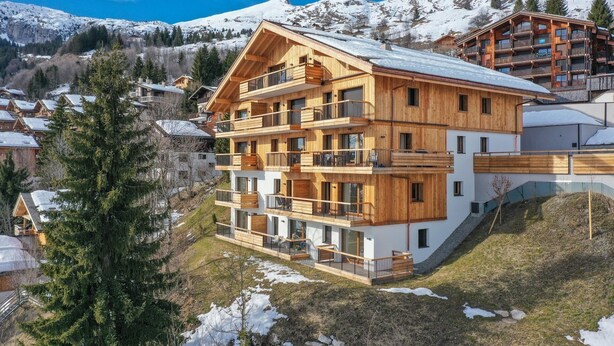 A multi-story wooden chalet with balconies, set in a snowy mountainous area.