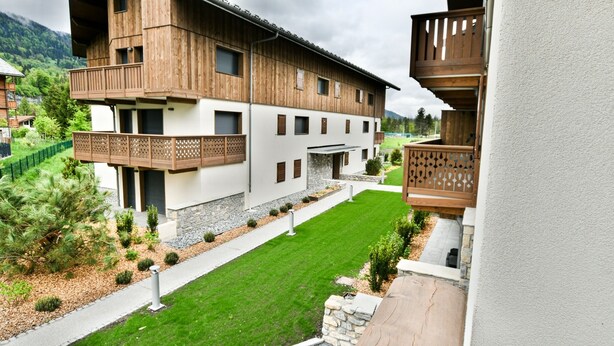 A multi-story building with wooden balconies, a stone foundation, and a well-maintained lawn. - Le Sève - B103 - One Bedroom Apartment, Sleeps 5 (Samoëns)