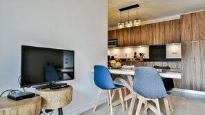 Moderni keittiö, jossa on puiset kaapit, ruokailutila kahdella tuolilla ja televisio puisen jalustan päällä.