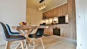 A modern kitchen with wooden cabinets, a built-in oven, and a dining area with a wooden table and chairs. - Le Sève - B103 - One Bedroom Apartment, Sleeps 5 (Samoëns)