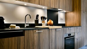 A modern kitchen with wooden cabinets, a black countertop, a stainless steel sink, and a built-in oven. - Le Sève - B103 - One Bedroom Apartment, Sleeps 5 (Samoëns)