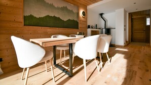 Un espace repas moderne avec une table en bois et des chaises blanches, une grande peinture représentant une forêt au mur et une cuisine en arrière-plan.