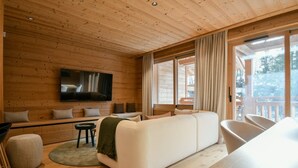 Un intérieur de chalet chaleureux avec un plafond en bois, un grand canapé, un téléviseur à écran plat et un coin repas.
