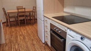 A compact kitchen with a washing machine, a small dining table with chairs, and a built-in oven. - 135A1 Charming Apartment in Gijón by R2R (Gijón)