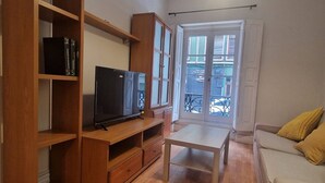 A living room with a wooden entertainment unit, a flat-screen TV, a sofa, and a window with a view of buildings. - 135A1 Charming Apartment in Gijón by R2R (Gijón)