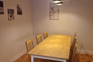 A dining area with a wooden table and chairs, a wall-mounted light fixture, and three framed pictures.