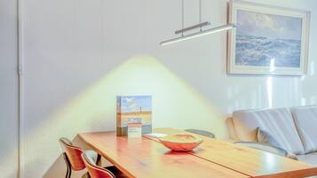 A dining area with a wooden table, chairs, a bowl, a framed painting, and a wall-mounted light fixture.
