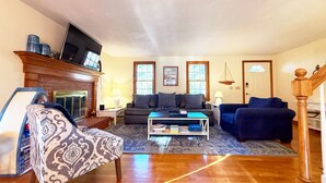 A living room with a fireplace, two sofas, a coffee table, and a patterned armchair. - Stevie, The Cape Farmhouse (Chatham)