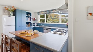 Une cuisine moderne avec des meubles bleus, un réfrigérateur blanc, un grand îlot central doté d’une cuisinière à gaz et une fenêtre donnant sur des collines.