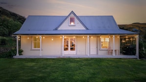 Une maison à deux étages avec un toit à pignon, une véranda à l’avant décorée de guirlandes lumineuses et une porte de garage bien visible.