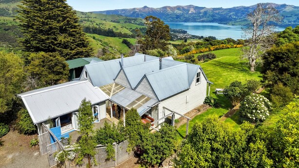 Une maison avec un toit en pente, entourée d’une végétation luxuriante et offrant une vue pittoresque sur des collines et un lac.