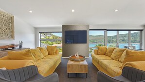 Een moderne woonkamer met twee gele banken, een houten salontafel en een grote flatscreen televisie die aan een gestreepte muur is bevestigd.