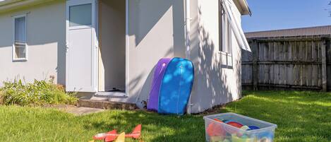 A house with a door open, a suitcase, and a container of toys on the grass.