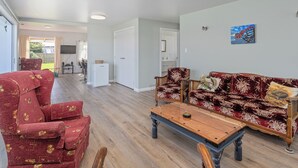 Un vaste espace de vie comprenant une table basse en bois, un canapé rouge à motifs et un fauteuil rouge. On aperçoit une table à manger et des chaises à l’arrière-plan.