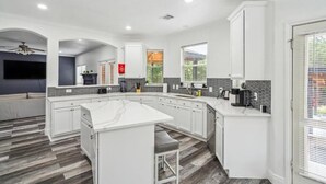 A modern kitchen with white cabinetry, a large island, and a herringbone-patterned floor. - Pool, Games & BBQ Luxury Texas Home 4 bedroom (San Antonio)