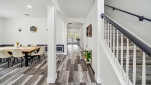 A modern interior with a dining area, a staircase, and a hallway leading to a door. - Pool, Games & BBQ Luxury Texas Home 4 bedroom (San Antonio)