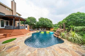Un patio trasero con una piscina de piedra, un porche cubierto y una pequeña cascada.