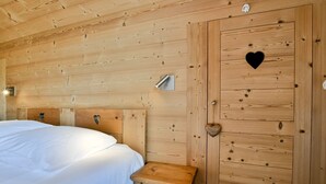 A wooden-paneled room with a bed, a bedside table, and a door with a heart-shaped cutout. - Chalet Anou - proche pistes de ski (Le Grand Bornand)