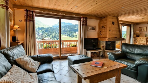 A cozy living room with a wooden ceiling, a black leather sofa, a wooden coffee table, and a TV. - Chalet Anou - proche pistes de ski (Le Grand Bornand)