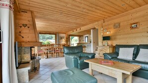 A cozy cabin interior with a stone fireplace, leather furniture, and a wooden ceiling. - Chalet Anou - proche pistes de ski (Le Grand Bornand)