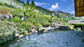 A gravel path leading to a wooden cabin with a satellite dish, surrounded by lush greenery and a mountain backdrop. - Chalet Anou - proche pistes de ski (Le Grand Bornand)