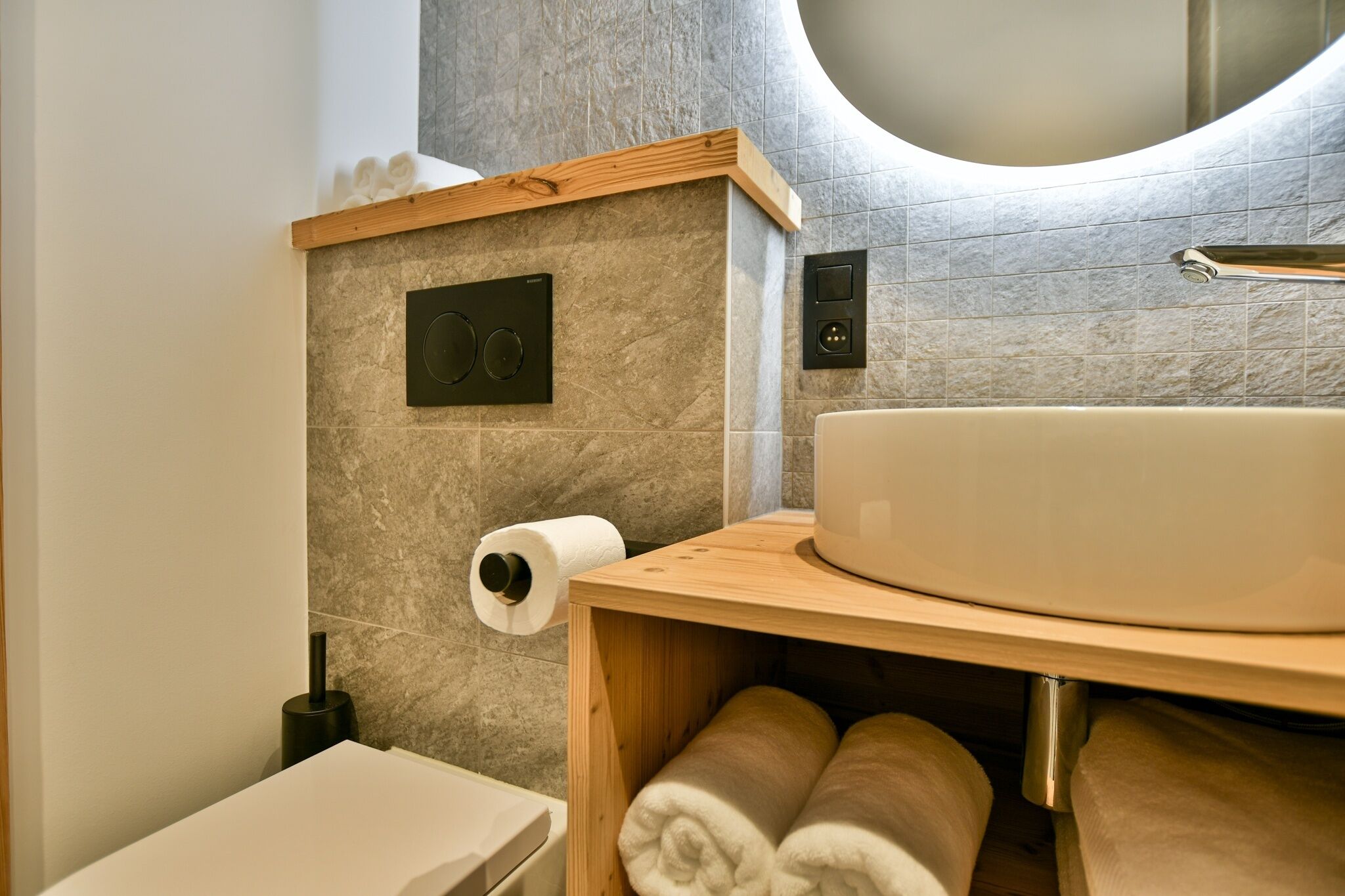 A modern bathroom with a wooden vanity, a large sink, a toilet, and a towel rack.