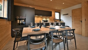 Een moderne keuken met donkere kastjes, een houten eettafel gedekt voor vier personen, en een groot raam.