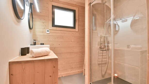 Un baño moderno con tocador de madera, cabina de ducha con mampara de vidrio y ventana sobre el lavabo.